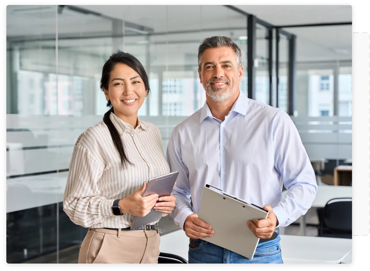 Two professionals standing in a conference room and smiling towards the camera