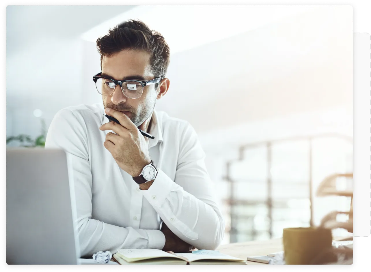 A man sitting in front of a computer with his left hand on his chin in a thinking position